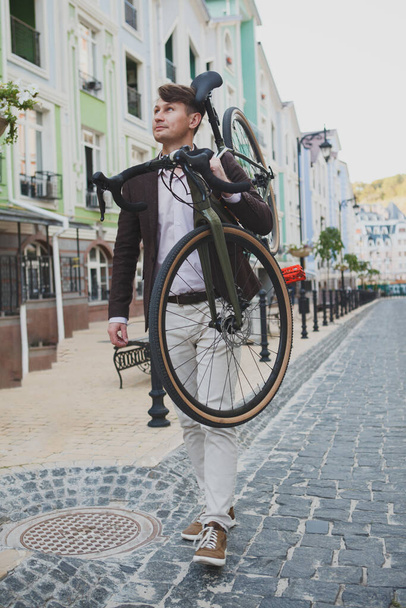 Vertical shot of a cheerful mature man enjoying warm autumn weather, walking in the city with his bike on his shoulder - Foto, Imagem