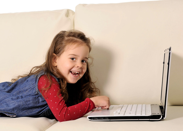 コンピューターと一緒に遊んでのソファの上に横たわるの幸せな女の子 - 写真・画像