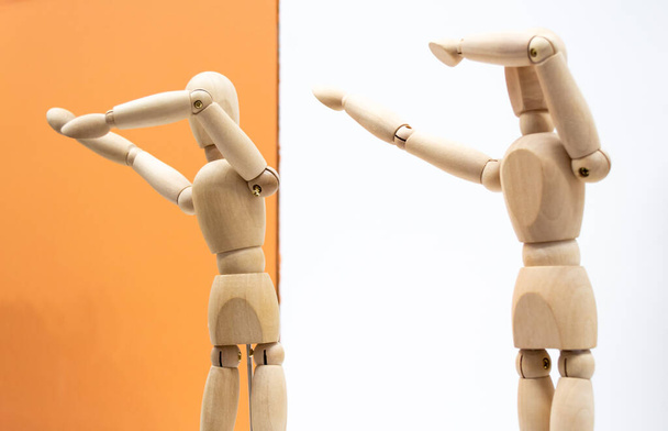 Two wooden human figures on white and orange backgrounds dance and make a deb movement - sneezing gesture. - Photo, Image