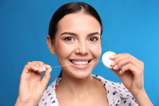 Young woman flossing her teeth on blue background. Cosmetic dentistry - Foto, imagen