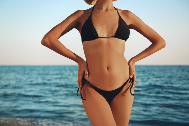 Woman in black stylish bikini on beach, closeup - Fotó, kép