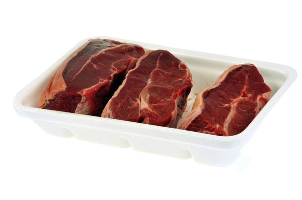 Pezzi di carne di manzo cruda in un vassoio di polistirolo primo piano su sfondo bianco - Foto, immagini