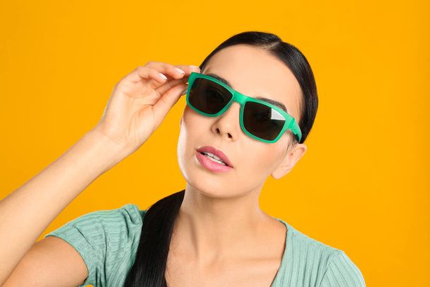 Beautiful woman wearing sunglasses on yellow background, closeup - Foto, afbeelding