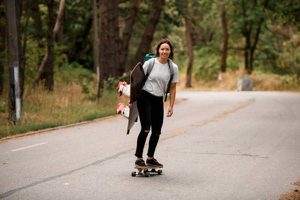 cheerful woman in white t-shirt riding skateboard with wakeboard in her hand. - Photo, Image