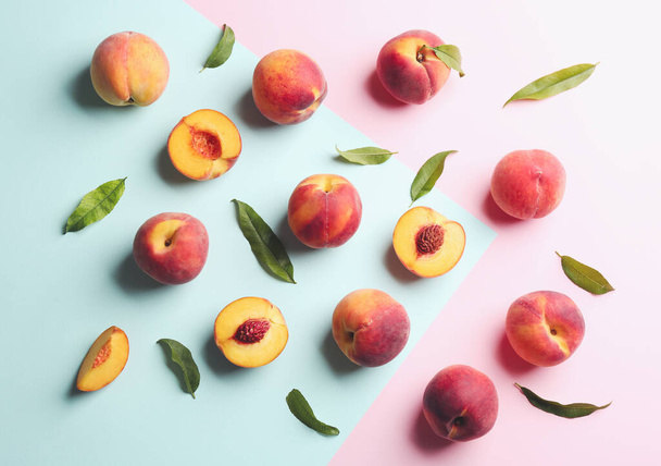 Fresh ripe peaches and green leaves on color background, flat lay - 写真・画像