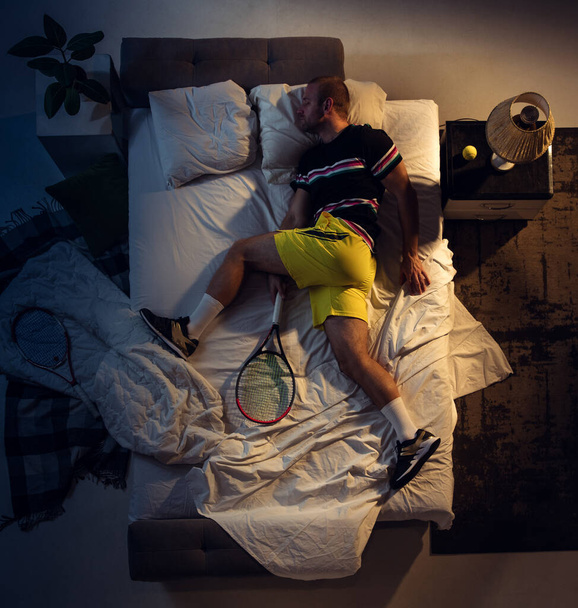 Top view of young professional tennis player sleeping at his bedroom in sportwear with racket - Fotó, kép