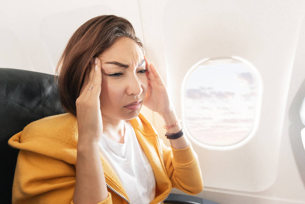 Tukehtuva aasialainen nainen lentää lentokoneessa ja yhtäkkiä tunsi voimakkaan migreenin ja päänsäryn. Terveystilanteen vuoksi matkustaja ei voinut helposti siirtää lentoa - Valokuva, kuva