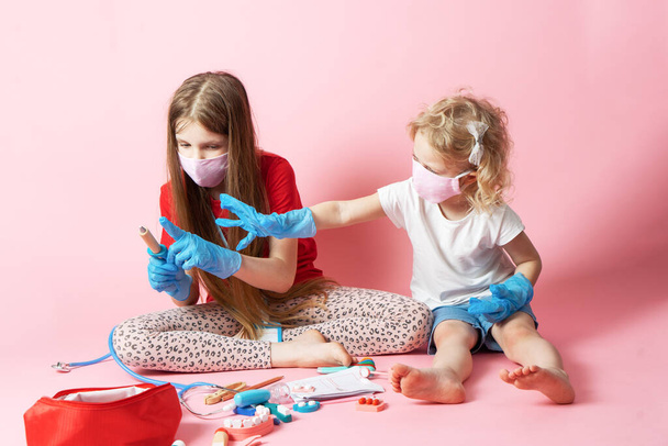 Personal protective equipment: two girls in medical masks and gloves play doctor and use a medical kit from toys. - Foto, imagen