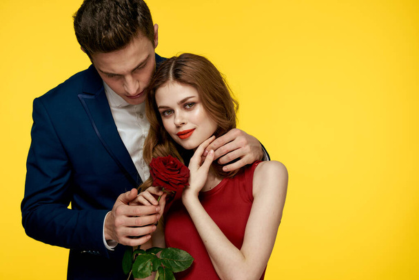 amoureux homme et femme avec une rose rouge dans leurs mains étreignant sur un fond jaune romance relation amour famille - Photo, image