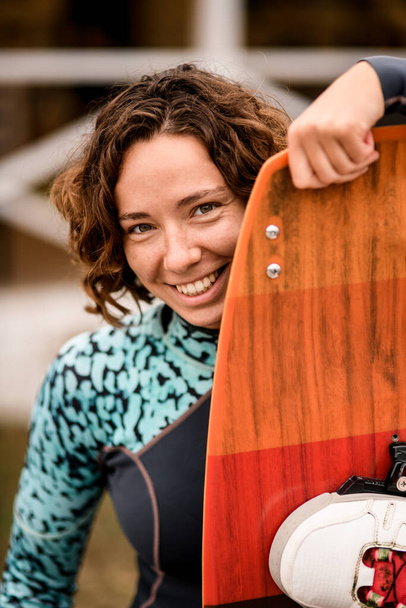 cheerful woman peeks out from behind wakeboarding board. - Φωτογραφία, εικόνα