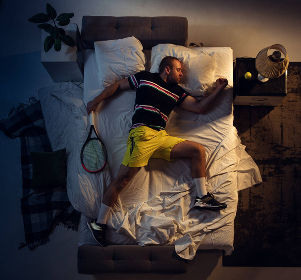 Top view of young professional tennis player sleeping at his bedroom in sportwear with racket - Photo, image