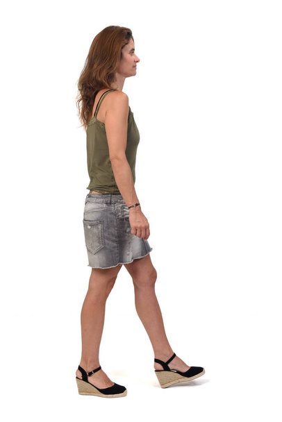 vista lateral del retrato completo de una mujer en una falda de mezclilla caminando sobre fondo blanco,  - Foto, imagen