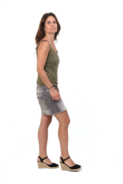 vista lateral do retrato completo de uma mulher em uma saia jeans andando sobre fundo branco,  - Foto, Imagem