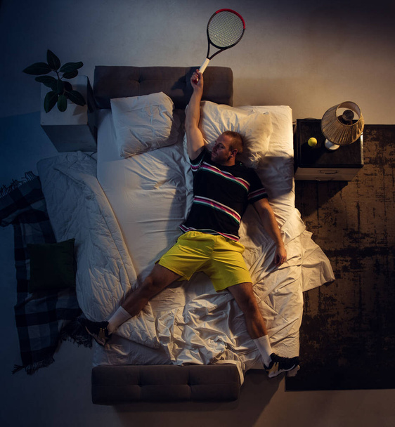 Top view of young professional tennis player sleeping at his bedroom in sportwear with racket - Foto, Bild