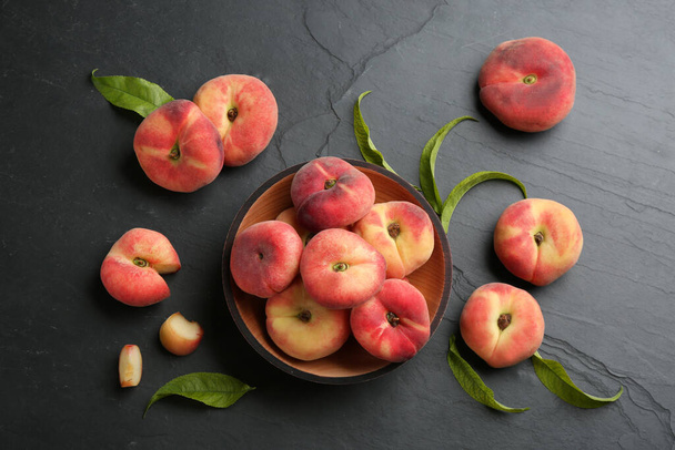 Fresh ripe donut peaches with leaves on dark table, flat lay - Фото, изображение