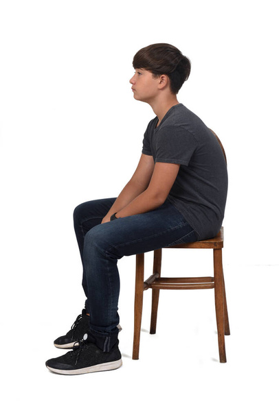 adolescent garçon assis sur une chaise avec fond blanc, regarder côté - Photo, image