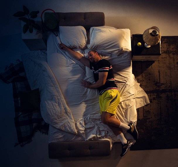 Top view of young professional tennis player sleeping at his bedroom in sportwear with racket - Zdjęcie, obraz