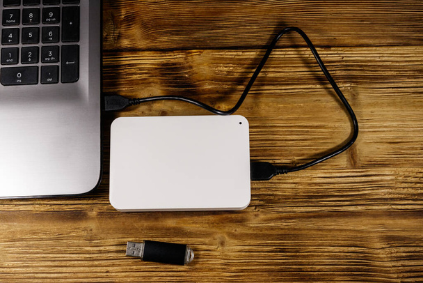 Внешний жесткий диск, подключенный к ноутбуку и USB флешке на деревянном столе. Вид сверху. Концепция хранения данных - Фото, изображение