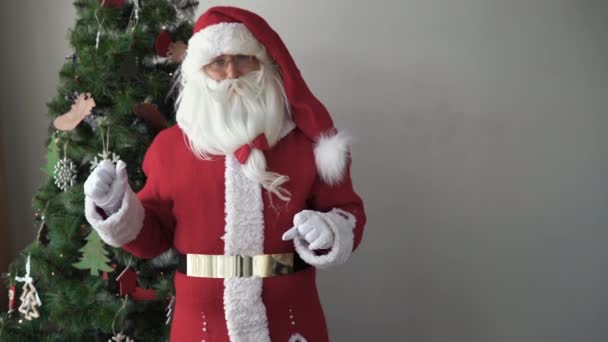 Der Weihnachtsmann steht neben dem Weihnachtsbaum und winkt mit dem Zeigefinger. Kindgerechtes Konzept - Filmmaterial, Video