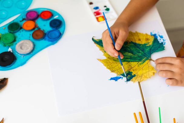 little girl paints leaves with brush at home, autumn art. - Photo, Image