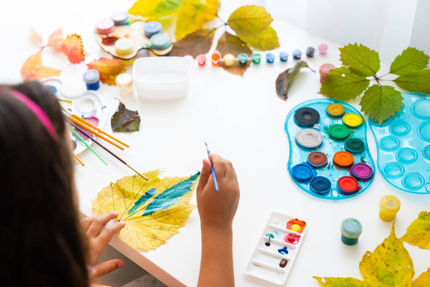 κοριτσάκι ζωγραφίζει φύλλα με πινέλο στο σπίτι, φθινοπωρινή τέχνη. - Φωτογραφία, εικόνα