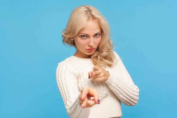 Angry depressed woman with curly blond hair pointing fingers at camera pretending to aiming gun, ready to make shot, difficulties. Indoor studio shot isolated on blue background - 写真・画像