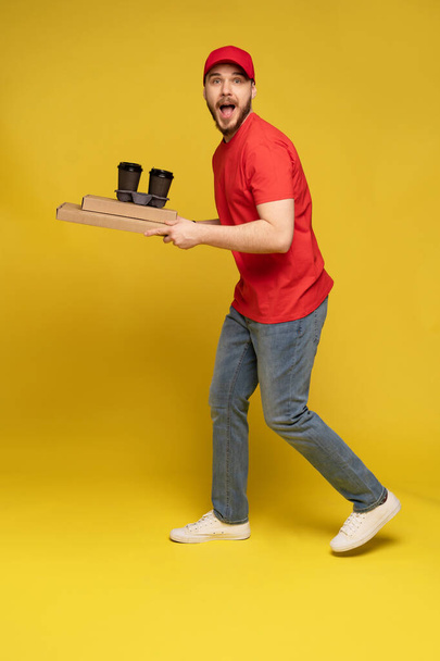 Delivery man in red cap, t-shirt uniform isolated on yellow background studio - Фото, зображення