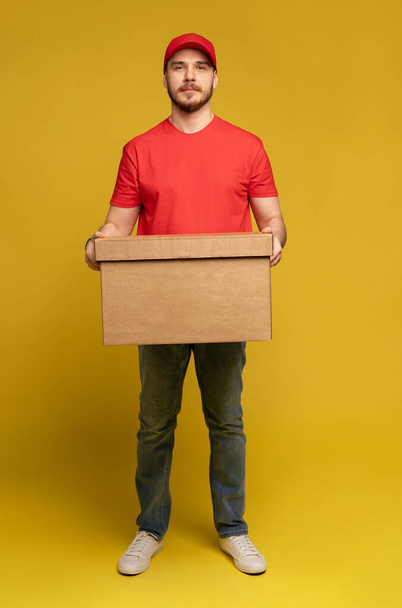 Delivery man with box in studio isolated on yellow background. - Fotoğraf, Görsel