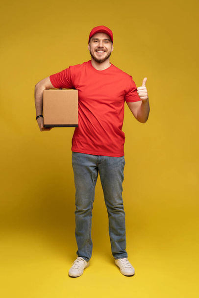 Delivery man with box in studio isolated on yellow background. - Фото, зображення