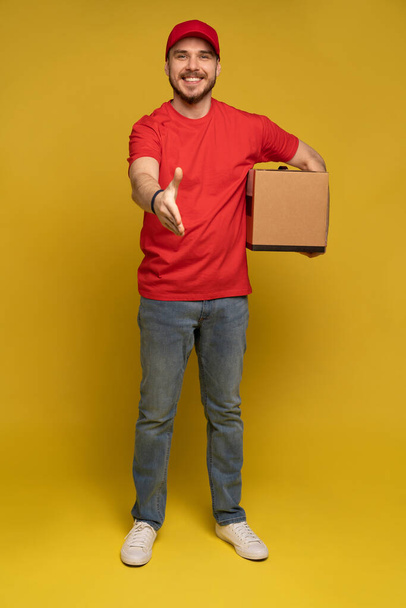 Delivery man with box in studio isolated on yellow background. - Photo, Image