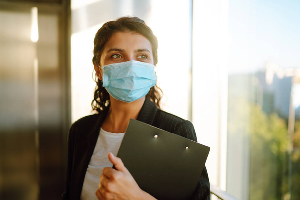 Young business woman wearing a face mask protect from infection of Covid-19 standing near elevator at office. Work during pandemic in quarantine city. - Foto, Imagem
