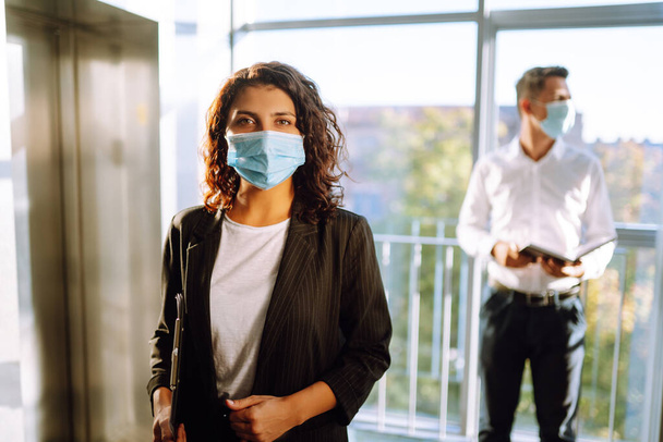 Young business woman wearing a face mask protect from infection of Covid-19 standing near elevator at office. Work during pandemic in quarantine city. - Φωτογραφία, εικόνα