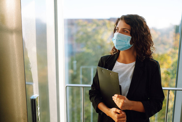 Young business woman wearing a face mask protect from infection of Covid-19 standing near elevator at office. Work during pandemic in quarantine city. - Foto, Imagem