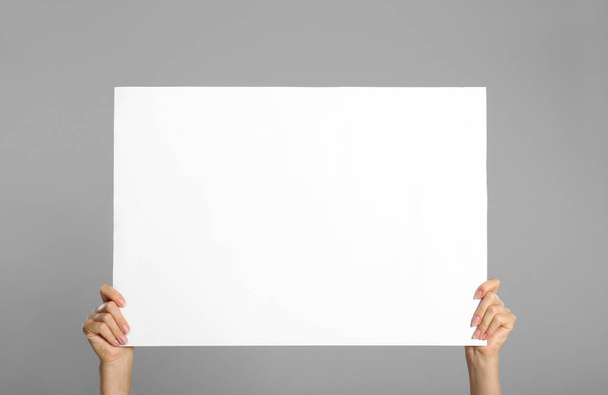 Woman holding white blank poster on grey background, closeup. Mockup for design - Photo, image