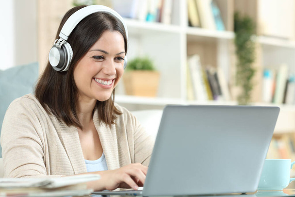 Happy woman with headphones using a laptop sitting in a desk at home - Fotó, kép