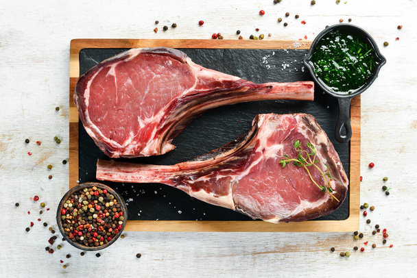 Dry aged raw tomahawk beef steak. Steak on the bone. On a white wooden background. Top view. Free copy space. - Zdjęcie, obraz