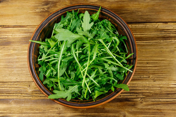Fresh green arugula in ceramic bowl on a wooden table. Top view. Healthy food or vegetarian concept - Photo, Image