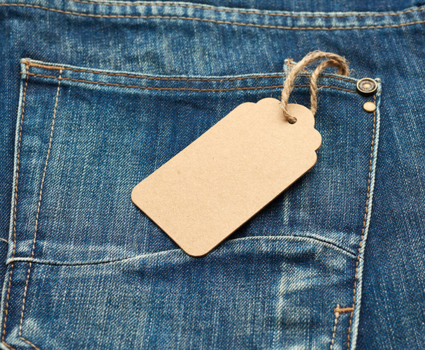 etiqueta rectangular marrón en blanco atada en el bolsillo trasero de vaqueros plegados azules, vista superior - Foto, imagen