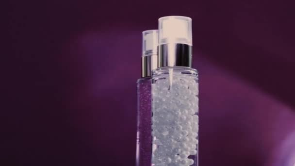 Meikkipohja ja seerumigeeli luksusihonhoitotuotteina ja kiiltävinä valosoihdutuksina violetilla pohjalla, ihonhoitorutiinina kasvojen kosmetiikassa ja kauneusmerkkinä - Materiaali, video