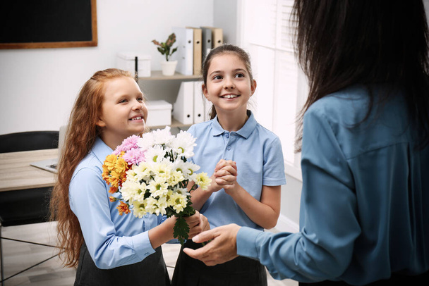 Schoolgirls congratulating their pedagogue with bouquet in classroom. Teacher's day - 写真・画像