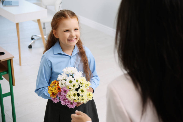 Schoolgirl with bouquet congratulating her pedagogue in classroom. Teacher's day - Фото, зображення