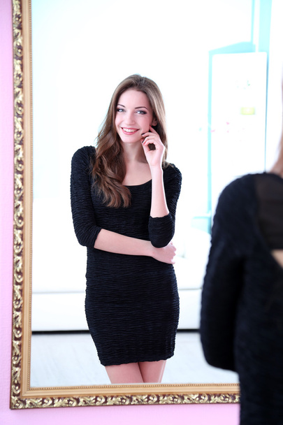 Young beautiful woman standing front of mirror in room - Fotó, kép
