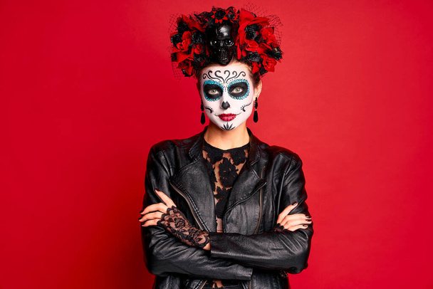 Young creepy lady calavera. wears artistic make-up for the feast of all the dead. dressed in a black leather jacket with a wreath of flowers on her head.Symbol of the Day of the Dead isolated in red - Photo, Image
