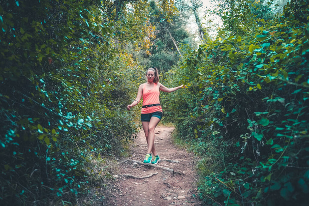 Beautiful young girl walking in forest. young happy attractive runner woman in jogging workout outdoors at countryside road track nature background running cheerful in healthy lifestyle concept. - Foto, imagen