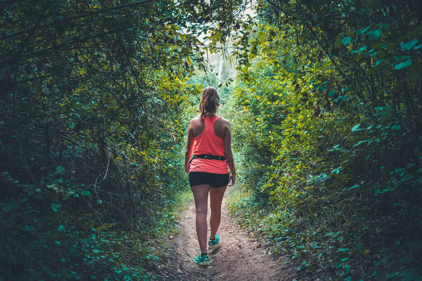 Beautiful young girl walking in forest. young happy attractive runner woman in jogging workout outdoors at countryside road track nature background running cheerful in healthy lifestyle concept. - Fotó, kép
