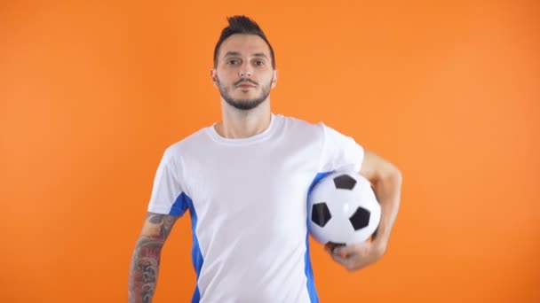 portrét tetovaného fotbalového fanouška nebo hráče držícího míč izolovaný na oranžovém pozadí - Záběry, video
