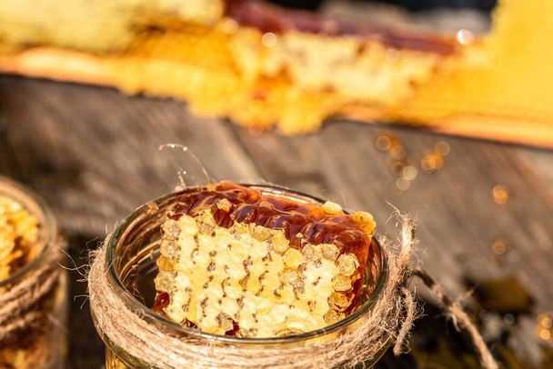 Φυσικό μέλι χτένα και ένα γυάλινο βάζο σε ξύλινο τραπέζι. Γλυκό φόντο. μελισσοκομικά προϊόντα με την έννοια των βιολογικών φυσικών συστατικών, closeup. - Φωτογραφία, εικόνα