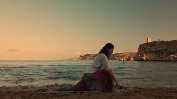Frau um die 40 praktiziert am frühen Morgen Yoga am Sandstrand. - Filmmaterial, Video