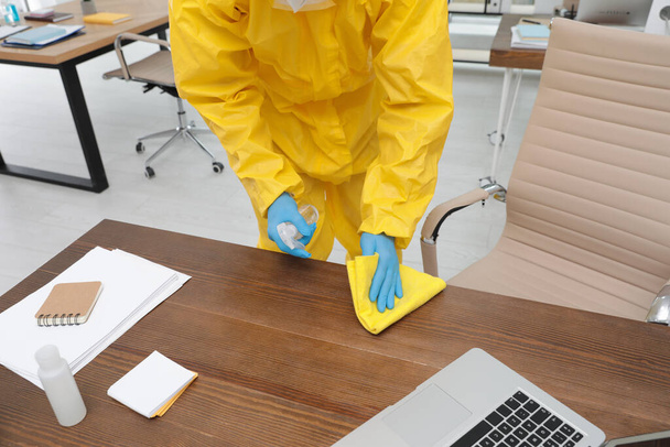 Janitor in protective suit disinfecting office furniture to prevent spreading of COVID-19, closeup - Foto, immagini