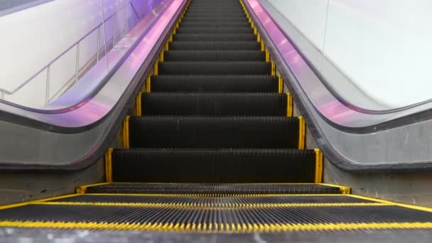 Vista en bucle de ángulo bajo de escaleras mecánicas modernas. Mecanismo de ascensor automatizado. Línea amarilla en escalera iluminada con luz púrpura. Escalera de maquinaria vacía futurista moviéndose recta - Imágenes, Vídeo
